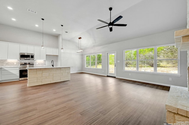 unfurnished living room with light wood-type flooring, ceiling fan, sink, high vaulted ceiling, and a fireplace