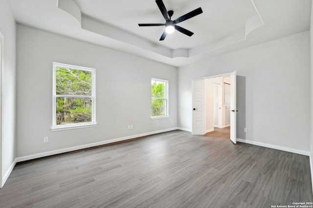 empty room featuring ceiling fan, a raised ceiling, wood-type flooring, and plenty of natural light