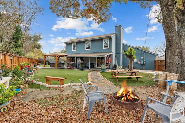 rear view of property featuring a gazebo, a hot tub, a fire pit, and a patio