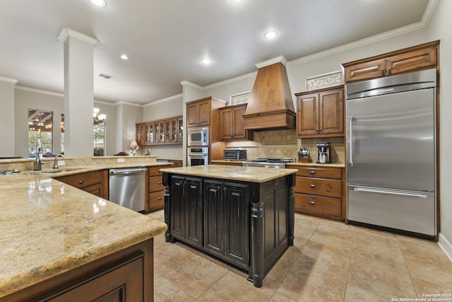 kitchen with premium range hood, built in appliances, light stone countertops, a notable chandelier, and a kitchen island