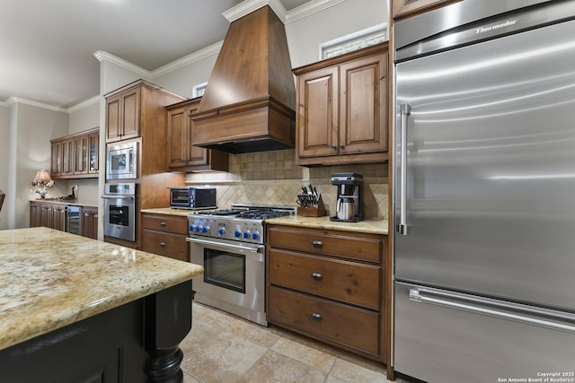 kitchen with built in appliances, light stone countertops, ornamental molding, tasteful backsplash, and custom range hood