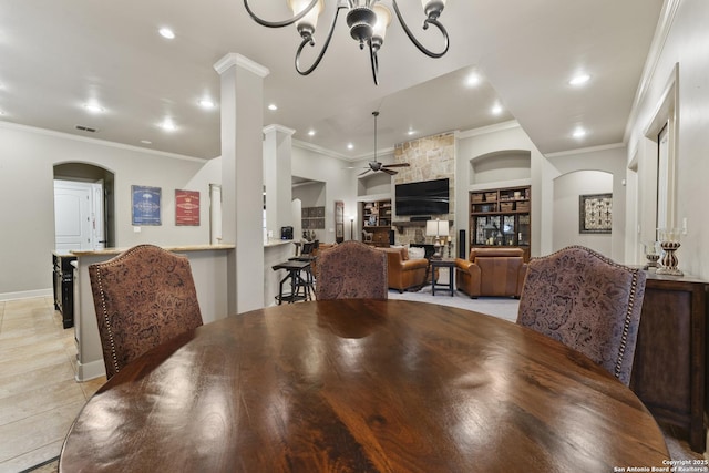 dining room featuring ceiling fan with notable chandelier, a stone fireplace, built in features, ornamental molding, and light tile patterned floors