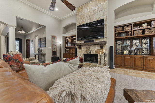 living room featuring built in shelves, ceiling fan, ornate columns, crown molding, and a fireplace