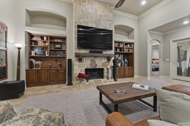 living room with built in shelves, a stone fireplace, and ornamental molding