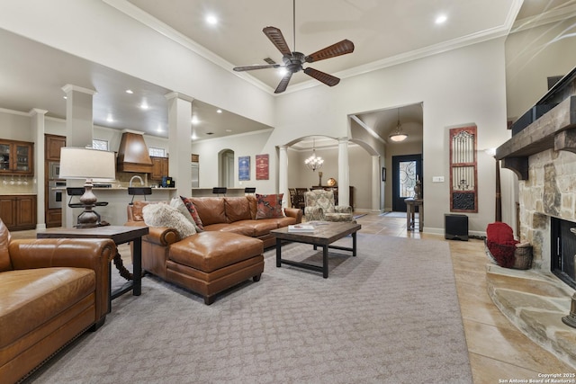 living room featuring decorative columns, a fireplace, light tile patterned floors, and ceiling fan with notable chandelier