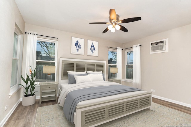 bedroom featuring a wall unit AC, multiple windows, ceiling fan, and wood-type flooring