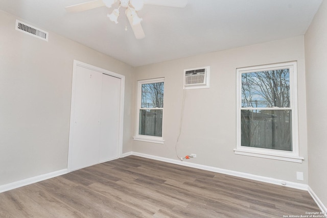 unfurnished room featuring hardwood / wood-style flooring, ceiling fan, a wealth of natural light, and a wall unit AC