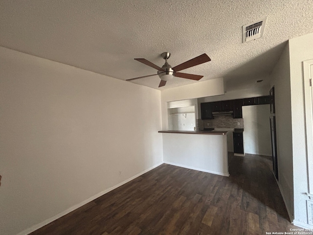 interior space with kitchen peninsula, backsplash, a textured ceiling, ceiling fan, and dark wood-type flooring