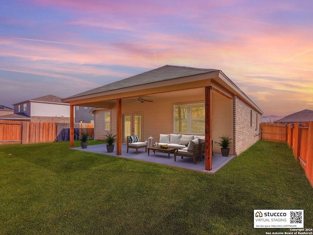 back house at dusk featuring an outdoor hangout area, ceiling fan, a patio area, and a lawn