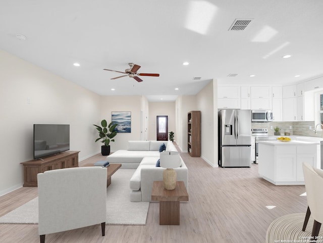 living room with light hardwood / wood-style floors, ceiling fan, and sink