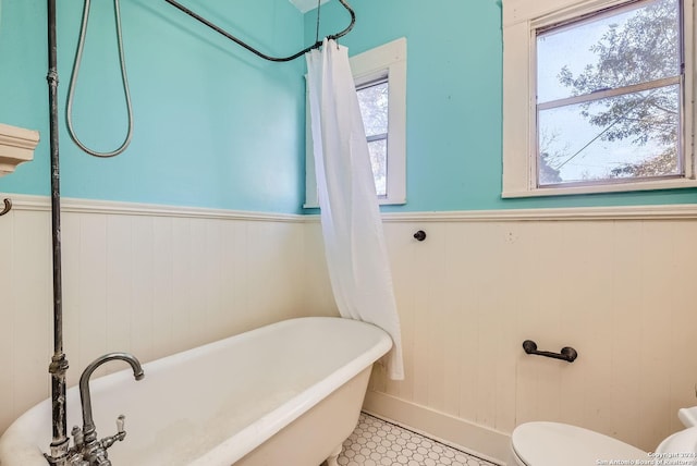 bathroom with a washtub, tile patterned floors, wooden walls, and toilet