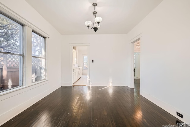 empty room with dark hardwood / wood-style flooring, plenty of natural light, and an inviting chandelier