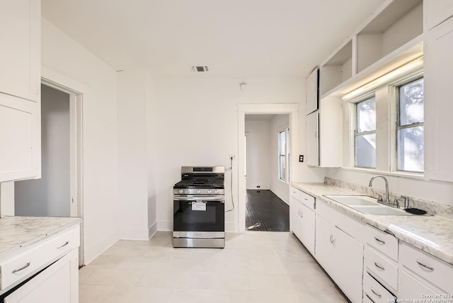 kitchen with stainless steel gas stove, light stone countertops, white cabinetry, and sink