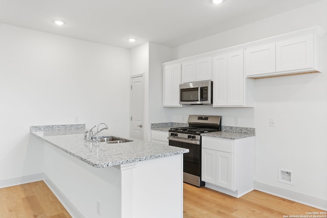 kitchen with a sink, appliances with stainless steel finishes, a peninsula, white cabinetry, and light wood-style flooring