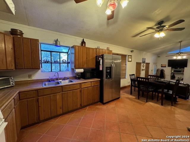 kitchen featuring ceiling fan, sink, stainless steel fridge with ice dispenser, lofted ceiling, and light tile patterned floors