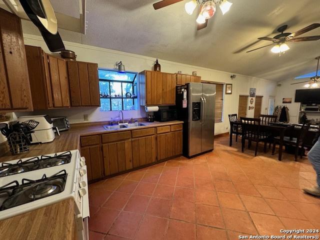 kitchen featuring stainless steel refrigerator with ice dispenser, white gas range oven, sink, lofted ceiling, and light tile patterned flooring