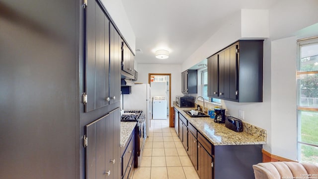 kitchen with sink, light tile patterned floors, light stone counters, stainless steel appliances, and washer / clothes dryer