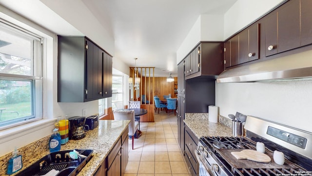 kitchen with light stone countertops, gas stove, wooden walls, light tile patterned floors, and hanging light fixtures