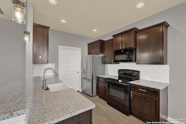 kitchen with a peninsula, a sink, light wood-style floors, light stone countertops, and black appliances