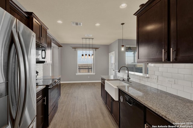 kitchen with light wood-style floors, light stone countertops, black appliances, pendant lighting, and a sink