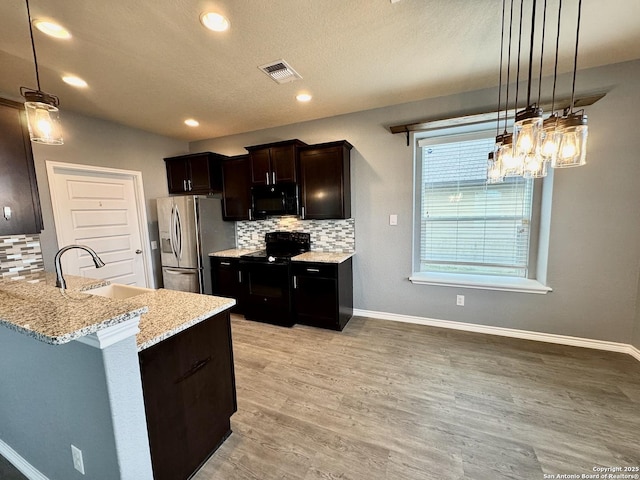 kitchen featuring visible vents, baseboards, light wood-style floors, hanging light fixtures, and black appliances