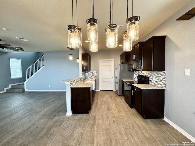 kitchen with light wood-style floors, backsplash, light stone countertops, black appliances, and pendant lighting