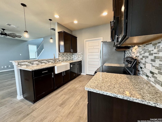 kitchen featuring a peninsula, a sink, black electric range, light stone countertops, and pendant lighting