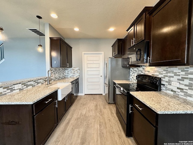 kitchen with light wood finished floors, decorative light fixtures, light stone countertops, black appliances, and a sink