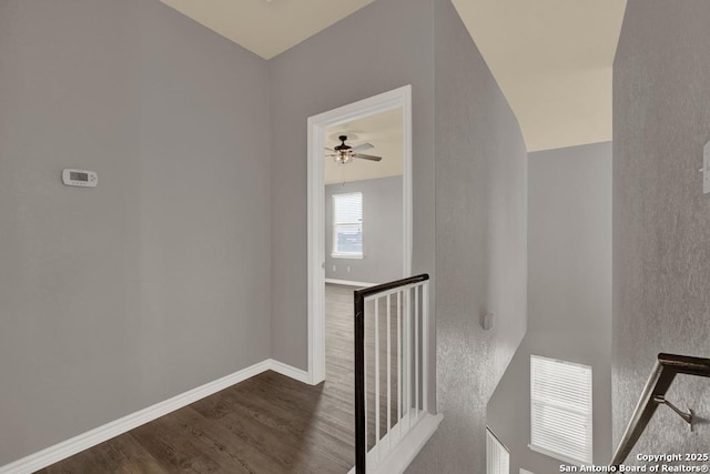 hallway featuring dark wood-style floors, an upstairs landing, visible vents, and baseboards