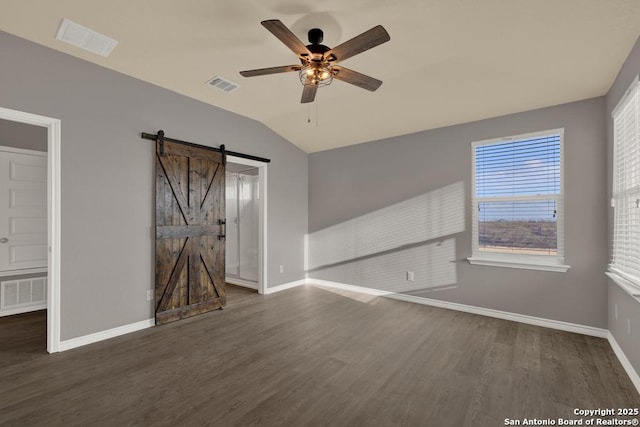 unfurnished room with dark wood-style flooring, visible vents, vaulted ceiling, and a barn door