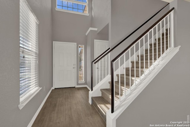 entryway with stairway, wood finished floors, a towering ceiling, and baseboards