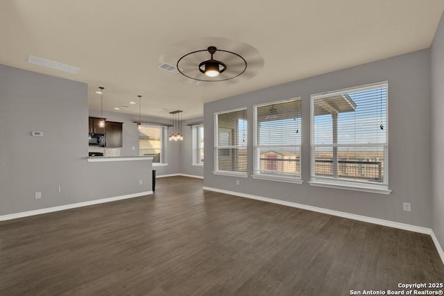 unfurnished living room with ceiling fan with notable chandelier, dark wood-type flooring, visible vents, and baseboards