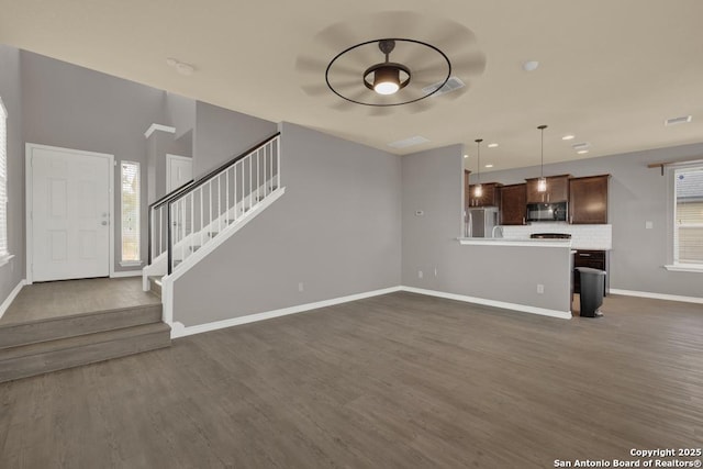 unfurnished living room with stairs, a healthy amount of sunlight, dark wood finished floors, and baseboards