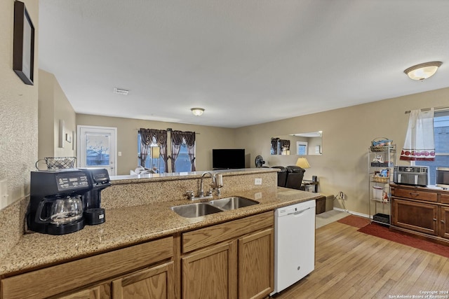 kitchen with dishwasher, light stone counters, sink, and light hardwood / wood-style flooring