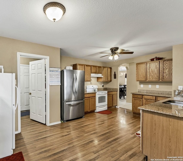 kitchen featuring stone counters, ceiling fan, sink, wood-type flooring, and white appliances