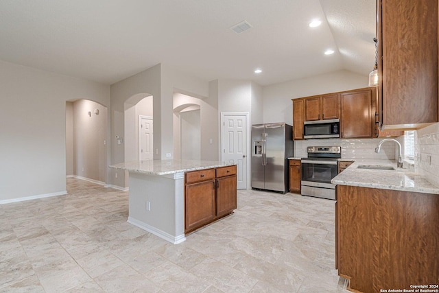 kitchen with backsplash, sink, light stone countertops, a kitchen island, and stainless steel appliances