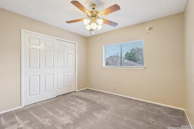 unfurnished bedroom with a textured ceiling, light colored carpet, a closet, and ceiling fan