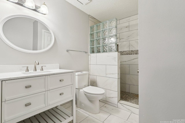 bathroom with tiled shower, vanity, a textured ceiling, and toilet