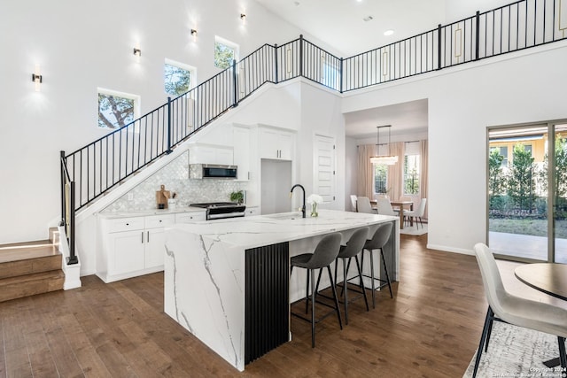 kitchen featuring appliances with stainless steel finishes, white cabinetry, a high ceiling, and an island with sink