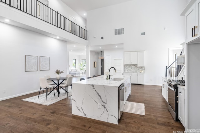 kitchen with white cabinetry, sink, a towering ceiling, a center island with sink, and appliances with stainless steel finishes