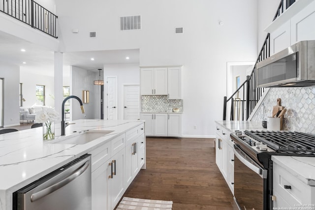 kitchen featuring sink, stainless steel appliances, tasteful backsplash, a towering ceiling, and white cabinets