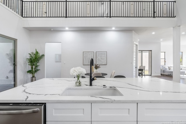 kitchen featuring a towering ceiling, light stone counters, sink, dishwasher, and white cabinets