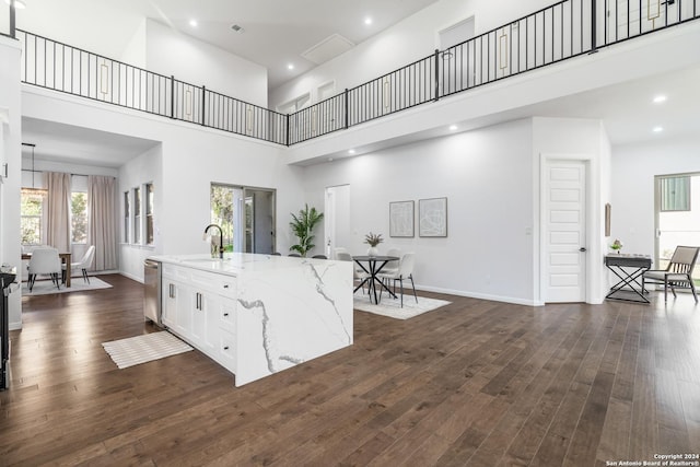 interior space with a high ceiling, white cabinets, stainless steel dishwasher, dark hardwood / wood-style floors, and an island with sink