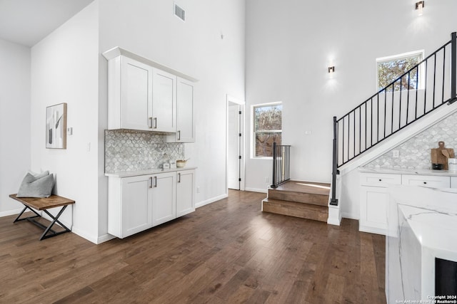 interior space with light stone countertops, a high ceiling, tasteful backsplash, and white cabinetry