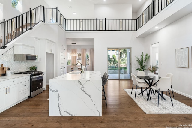 kitchen featuring a towering ceiling, stainless steel appliances, a center island with sink, and sink