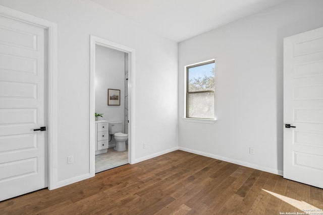 unfurnished bedroom with ensuite bathroom and dark wood-type flooring