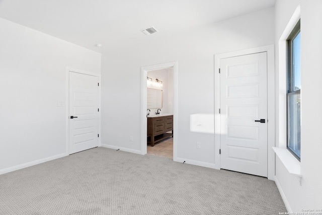 unfurnished bedroom featuring light carpet, connected bathroom, and multiple windows