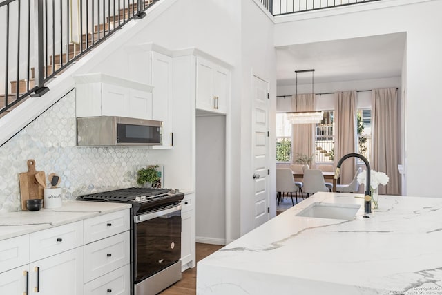 kitchen with light stone counters, stainless steel appliances, sink, white cabinetry, and hanging light fixtures