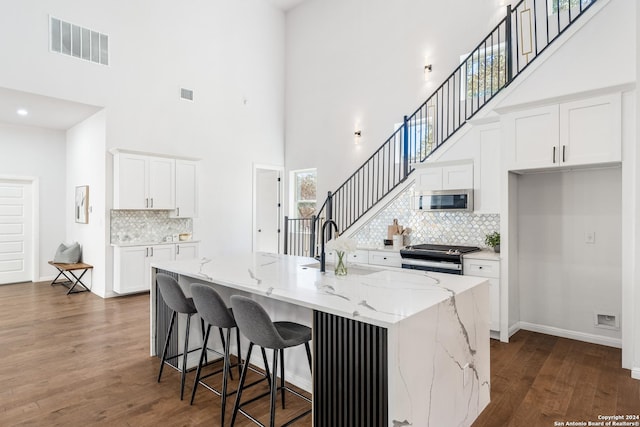 kitchen with a high ceiling, stainless steel appliances, white cabinetry, and an island with sink