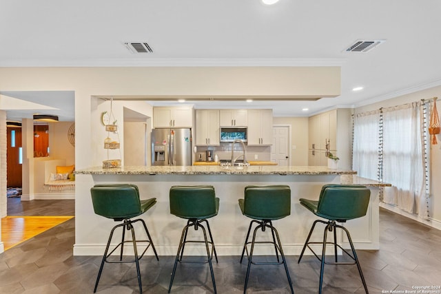 kitchen with a kitchen breakfast bar, light stone countertops, ornamental molding, and stainless steel refrigerator with ice dispenser